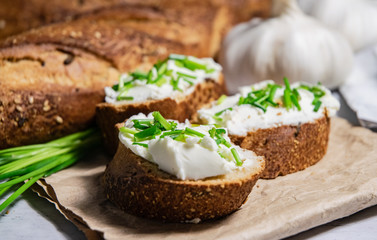 Pieces of French baguette with fresh green chives, white curd spread placed on rustic paper