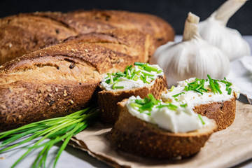 Pieces of French baguette with fresh green chives, white curd spread placed on rustic paper