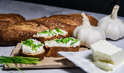 Pieces of French baguette with fresh green chives, white curd spread placed on rustic paper