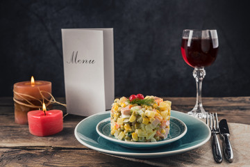 Russian salad on a blue plate, canteens and a glass of wine on the table.
