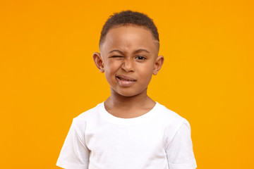 Children, fun and body language concept. Cute African American little boy grimacing against yellow...