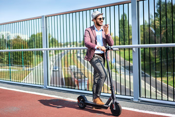 Young man standing on motorized scooter in the city and talking on phone