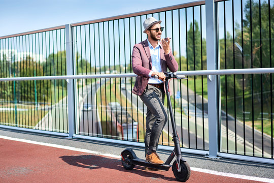 Young Man Standing On Motorized Scooter In The City And Talking On Phone