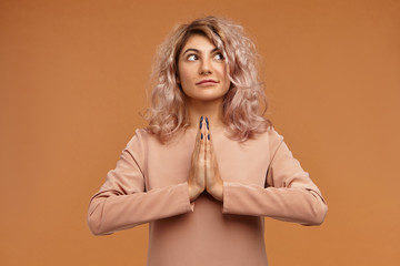 People, peace, meditation and zen concept. Picture of fashionable young female with nose ring and curly hair holding hands in namaste, meditating, trying to calm down her restless mind and relax