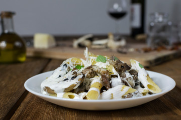 Italian pasta penne with salsiccia sausage, mushrooms, cheese and cream on wooden table.