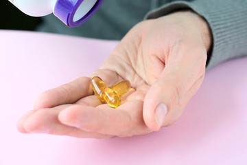 Yellow omega 3 vitamin capsules in male palm. Man holding omega 3 soft gel pills with selective...