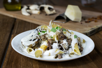 Italian pasta penne with salsiccia sausage, mushrooms, cheese and cream on wooden table.