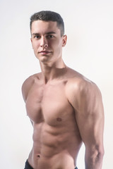 Fototapeta premium Beautiful young European athletic with bare torso, nice abs and muscles on white and gray background
