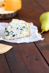 Various types of cheese and pear on wooden boards. Slices of cheese on blurred background. Dorblu, camembert and hard yellow cheese on parchment paper