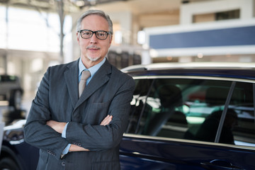 Car dealer salesman in front of a car in his showroom