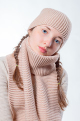 Beautiful girl with blue eyes and wicker braids in a knitted hat and scarf. Light background, Cheerful look in the camera