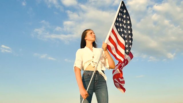 Pretty girl teenager  stand with American flag against blue sky. Slow motion