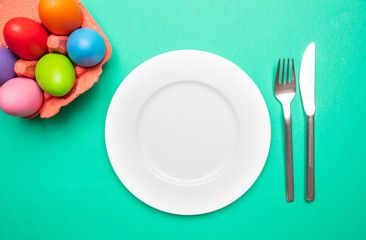Easter table, place setting. Easter eggs,  empty white plate, green background