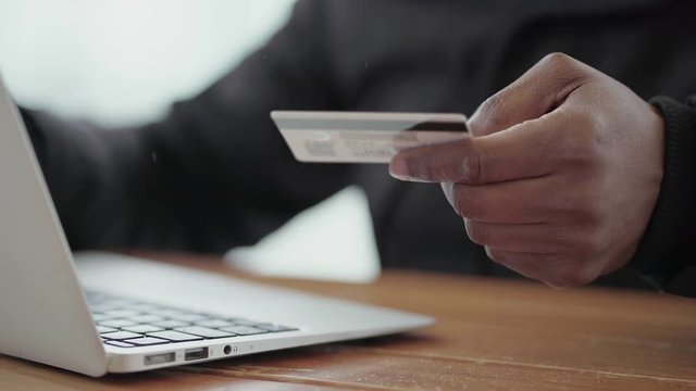 Afro-American middle-aged male hand buying goods from internet on laptop with credit card. Close-up shot, side view. Modern technology concept. 
