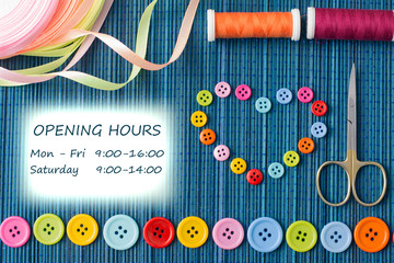 Opening hours door sign of a tailoring shopt: heart made of small buttons, row of colorful buttons, threads, scissors,  ribbons on a dark blue straw mat