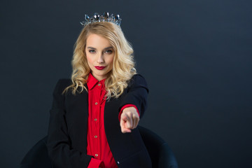 beautiful young girl in a black jacket sits in a chair with a crown on her head on a black background