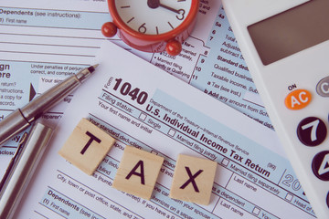 Tax with wooden alphabet blocks, Red alarm clock, calculator and pen on 1040 tax form backgrounda