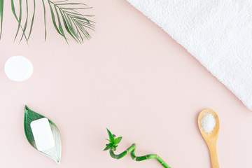 Flat lay and top view of white towel, jar of cream, green palm leaves and bamboo on pastel pink...