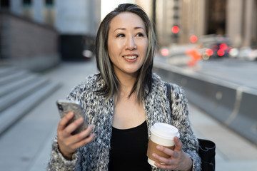 Asian woman in city walking texting cell phone