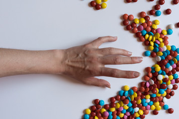A hand pulls for colorful chocolate coated candy on white background. Unhealthy nutrition concept