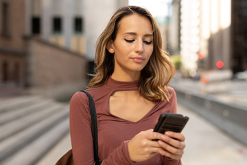 Young woman in city walking texting on cell phone
