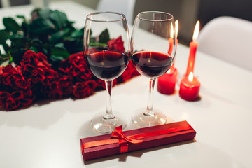 Celebrating Valentine's Day with wine, candles, roses and gift box at home. Romantic atmosphere for lovers