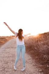 young woman raising arms at sunset in the field