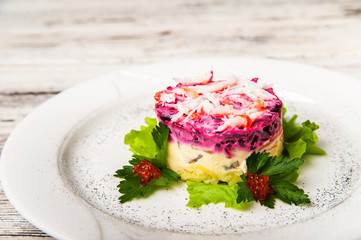 Herring salad under a fur coat with crabs on a white plate. Traditional Russian cuisine, herring under a fur coat close-up and copy space.