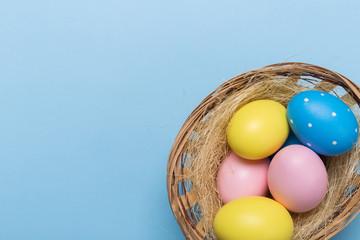Colorfull easter eggs in nest on blue pastel color background with space.