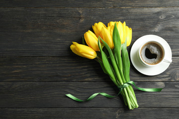 Beautiful yellow tulips and cup of coffee on wooden background, space for text