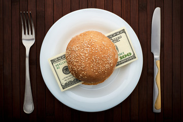 Conceptual photo. Hamburger with one hundred dollar bills. On a white plate. Near fork and knife. Top view. - 248518906