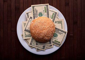 Conceptual photo. Hamburger with dollars on a white plate and on a wooden background. Top view.. - 248518916