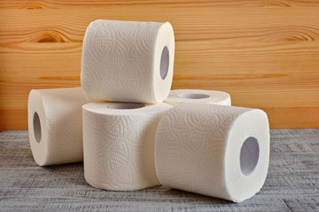 Rolls of white toilet paper on white and wooden background
