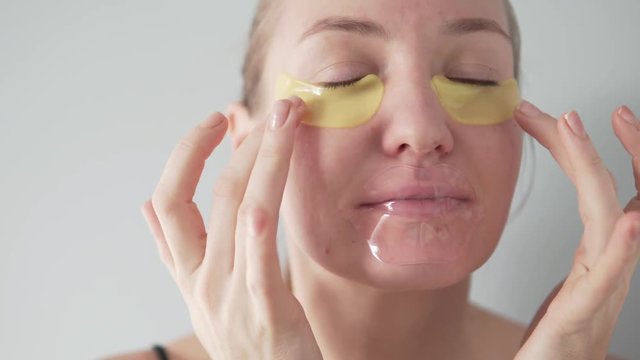 Young woman caring for the skin of the face. She applies a moisturizing mask under the eyes. Silicone patch on lips