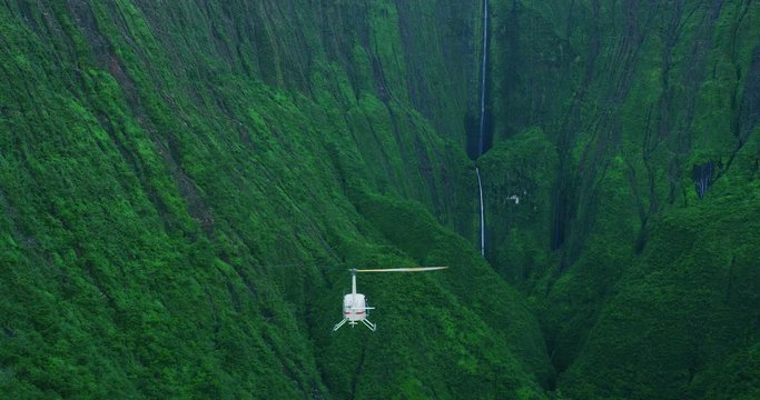 Aerial shot of helicopter approaching giant waterfall in lush green valley, epic helicopter adventure