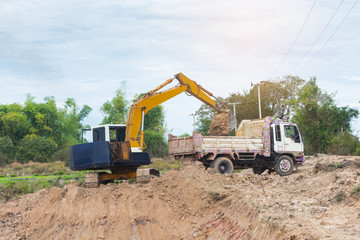 Yellow excavator machine loading soil into a dump truck at construction site