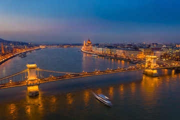 Fototapeta na wymiar Budapest, Hungary - Aerial view of the famous illuminated Szechenyi Chain Bridge at blue hour with sightseeing boat on River Danube and Parliament at the background
