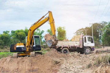 Yellow excavator machine loading soil into a dump truck at construction site