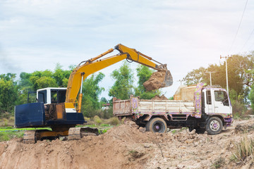 Yellow excavator machine loading soil into a dump truck at construction site