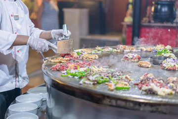 The cook in the restaurant fries food on a large iron oven.