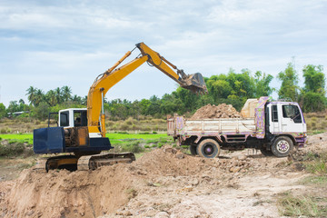 Obraz premium Yellow excavator machine loading soil into a dump truck at construction site