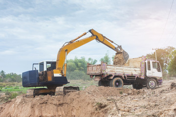 Obraz premium Yellow excavator machine loading soil into a dump truck at construction site