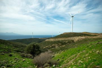 Fototapeta na wymiar View of wind turbines on the top of mountains of a green nature under a cloudy but bright sky