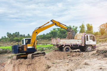 Yellow excavator machine loading soil into a dump truck at construction site