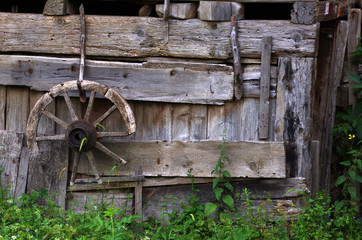 a broken wooden cart wheel hang on a wooden wall of a house