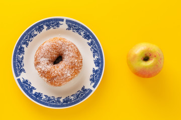 A plate with sugar coated doughnut and an apple , on yellow background.