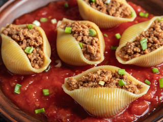 cooked pasta conchiglioni stuffed minced meat, tomato sauce close up