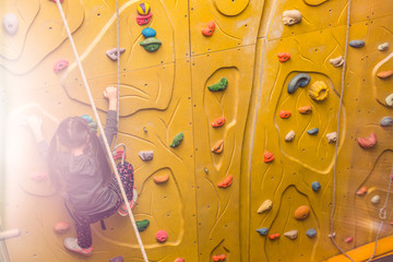 Little girl climbing a rock wall indoor