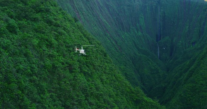 Aerial view of helicopter flying towards giant waterfall in amazing lush green valley, epic helicopter adventure, slow motion