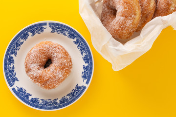 A plate with sugar coated doughnut , on yellow background.